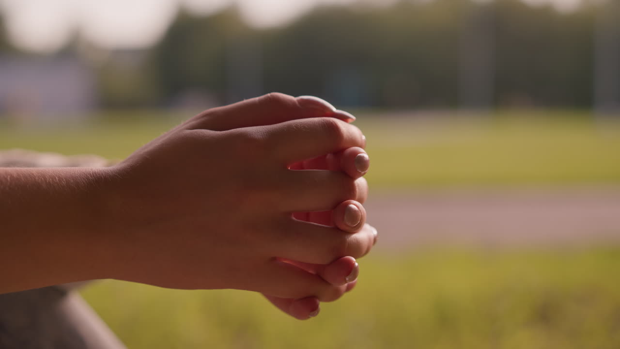 Close-up of individual clasping hands together in a relaxed, thoughtful pose against blurred background of lush green landscape and distant trees