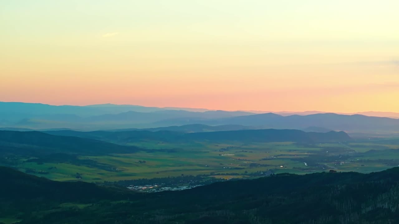 Wide aerial of Steamboat Springs ridges and valleys lit by soft golden sunlight at dusk, blue hour dusk backdrop