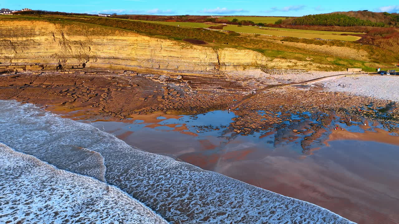 Aerial view of wave-cut platform and tide pools at Southerndown. Downward drone shot of rocky beach formations, tide pools, and limestone strata at Dunraven Bay beach