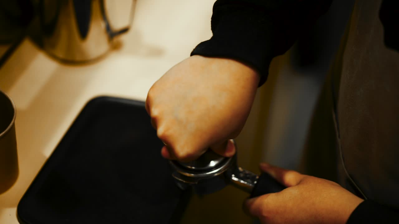 Nærbillede fra høj vinkel af barista, der presser kaffegrums ned i et portafilter