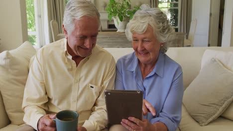 Pareja-Mayor-Caucásica-Sonriendo-Mientras-Usa-Una-Tableta-Digital-Juntos-Sentados-En-El-Sofá-En-Casa