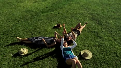 three attractive girls lying on green grass and having fun on a meadow sunny day and background of mountain