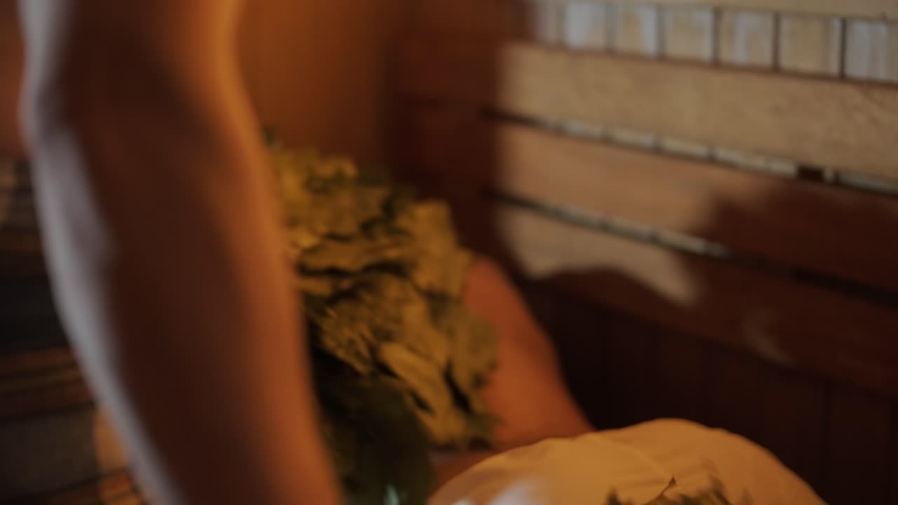 스파에서 나무 벤치에 누워있는 남자와 마사지 마사지하는 오크 자루와 함께 핀 사우나에서 실내에서 전문가와 함께 클라이언트.