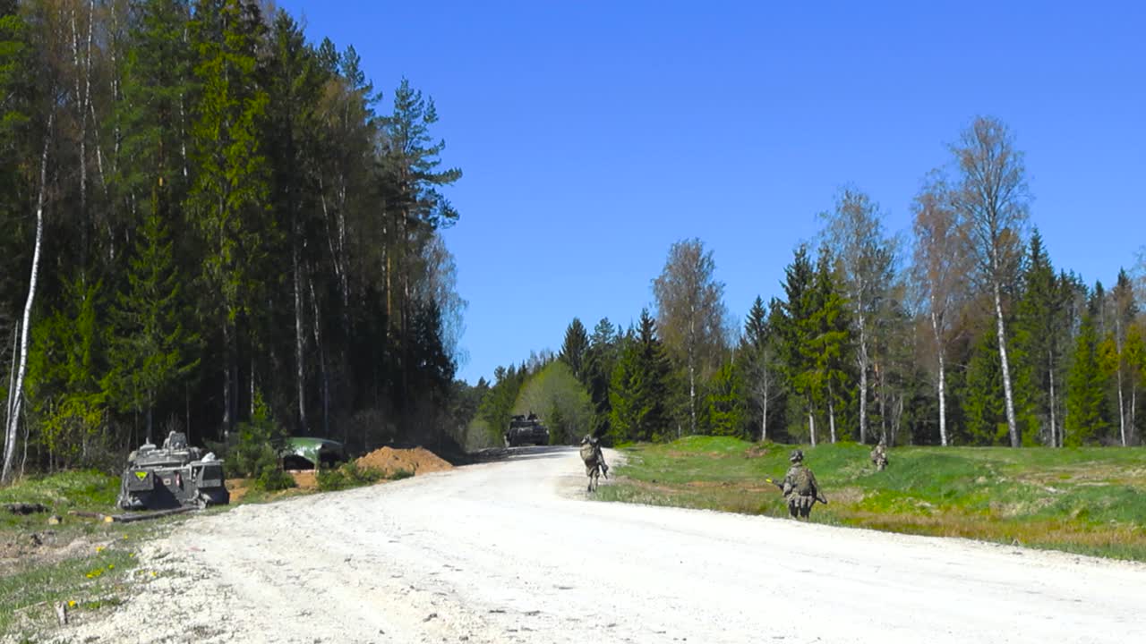 Rare video footage of British infantry platoon military or army soliders preforming a mission by walking and patrolling a rural gravel white dusty countryside road in a sunny pine forest, armed forces