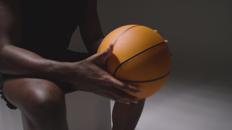 Studio-Nahaufnahme: Sitzender männlicher Basketballspieler mit Ball in den Händen 3