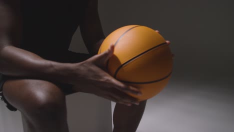 close up studio shot of seated male basketball player with hands holding ball 3