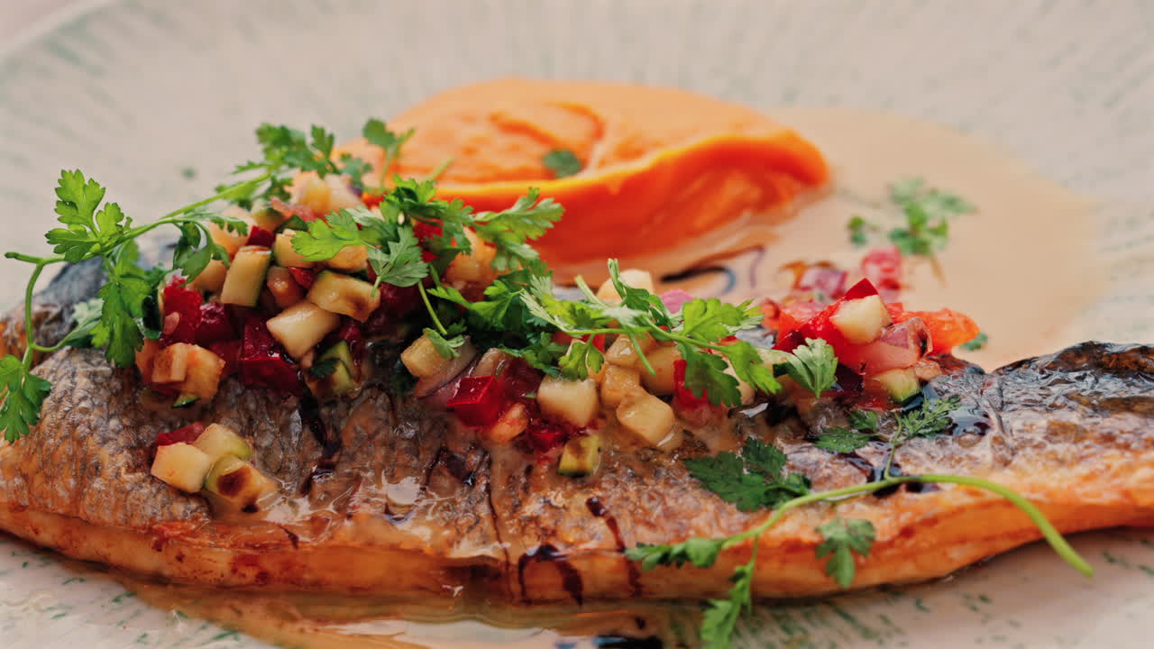Close up of grilled fish with a sweet potato puree and a sauce on a white plate on a table at a restaurant