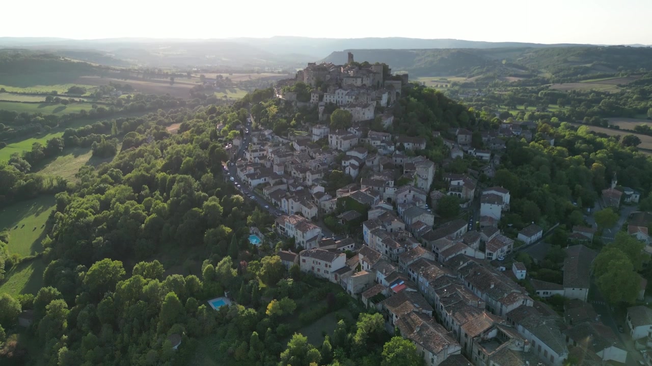 Vista aerea con drone nella campagna francese di una piccola e antica città medievale in mattoni su una cima di montagna circondata da campi verdi, con una lenta ascesa verticale in una giornata di sole a Cordes Sur Ciel.
