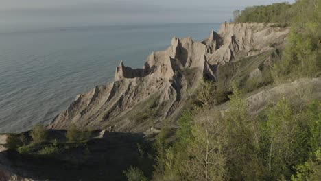 drone shot, flying forward, panning up and to the right, revealing a carved out rock formation by the weather, down by the coastline of a lake