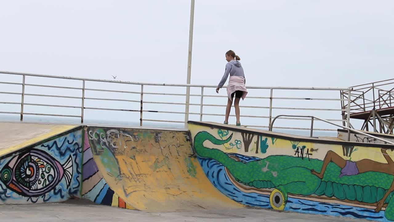Girl Skateboarding on a Graffiti-Covered Ramp at a Coastal Skatepark