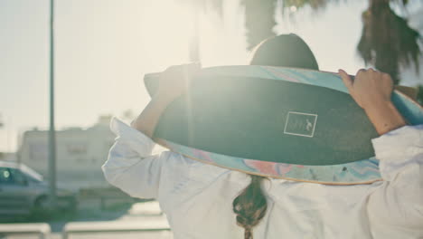 portrait happy skater holding longboard walking promenade. woman looking camera