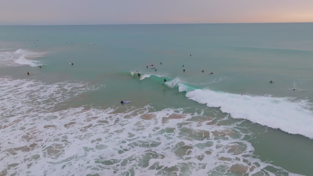 los surfistas entran, tallan y montan en hermosas olas bajo un cielo pastel, cámara lenta
