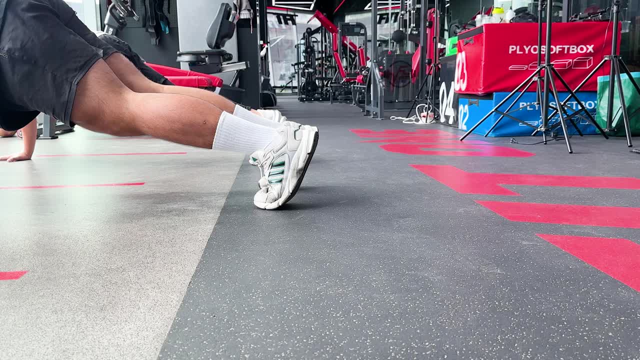 Person executes mountain climbers on gym floor, bright lighting, low angle, dynamic movement, fitness focus