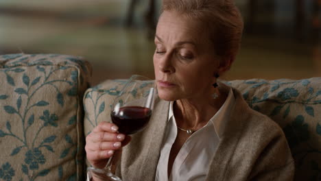 mujer anciana tranquila bebiendo un vaso de vino rojo en el interior