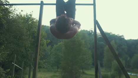 young fit topless male doing sit up exercise for strengthening core upside down on pull ups bar outdoors