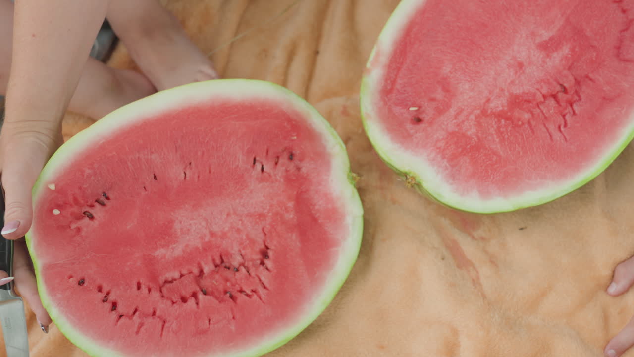 Closeup of woman preparing juicy watermelon, Relaxed summer picnic with woman cutting sweet watermelon, Barefoot woman enjoying peaceful summer picnic by slicing ripe watermelon on towel
