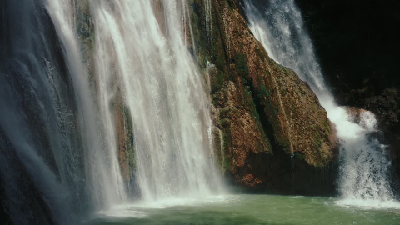 Ground-level shot of powerful waterfall plunging into a pool, framed by dark cliffs and mist rising from the surface