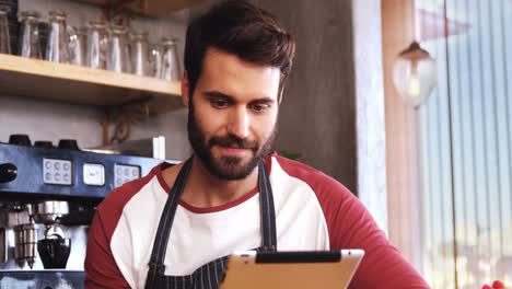 Smiling-waiter-using-digital-tablet-at-counter-in-cafe