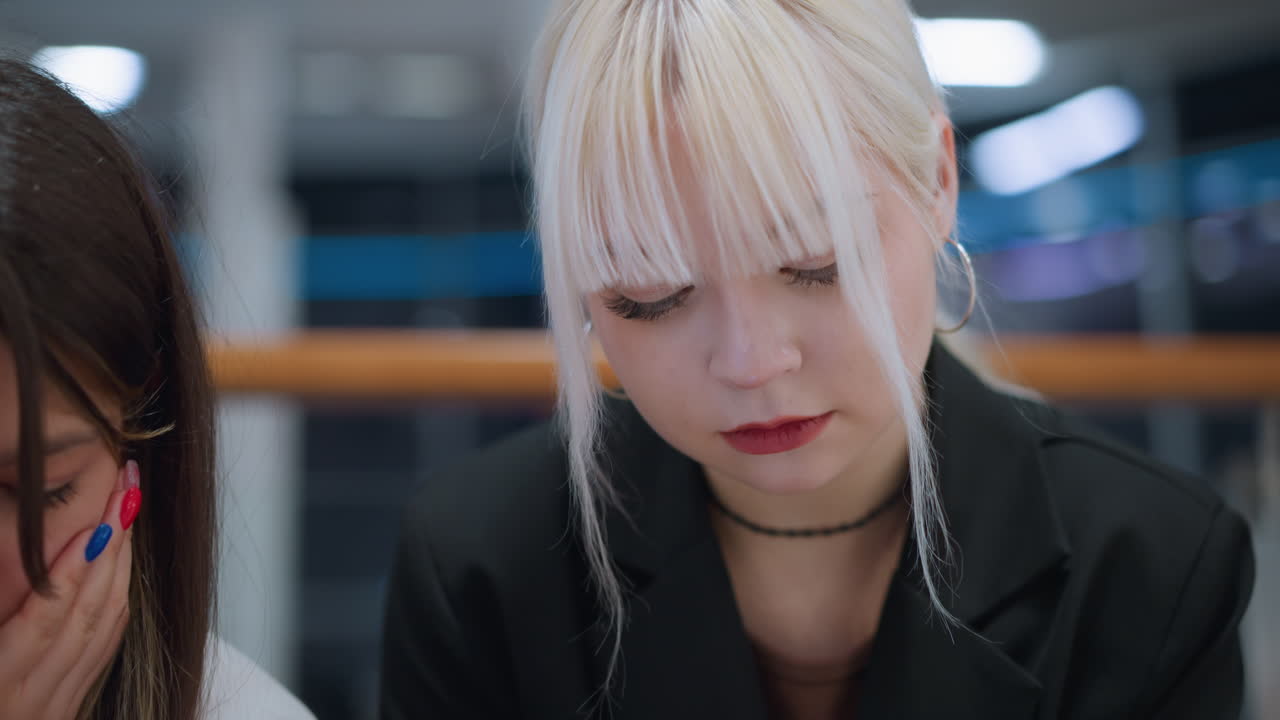 High school girls sitting indoors operating phone while chatting showing focused expressions symbolizing youth connection, social interaction and digital lifestyle