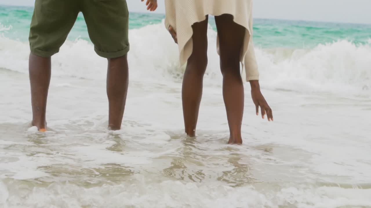 sección baja de una pareja afroamericana jugando con las olas del mar en la playa 4k
