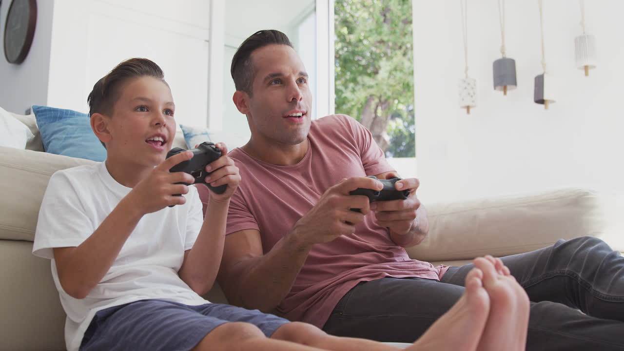 padre e hijo hispanos sentados en el suelo en casa jugando videojuegos juntos