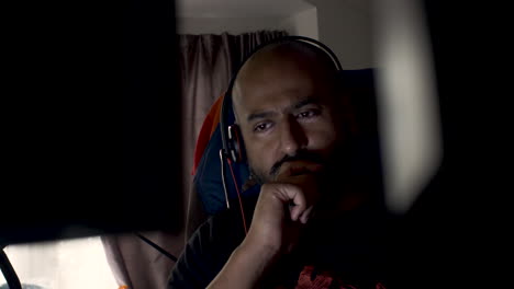 Pensive-UK-Asian-Male-Wearing-Headset-Working-From-Home-Swaying-Side-To-Side-On-Chair