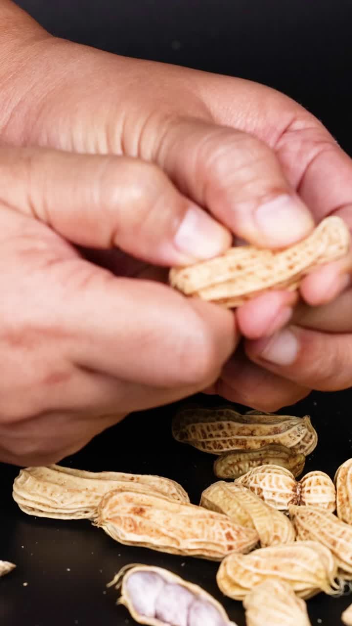 manos cuidadosamente pelando cacahuetes en un fondo negro