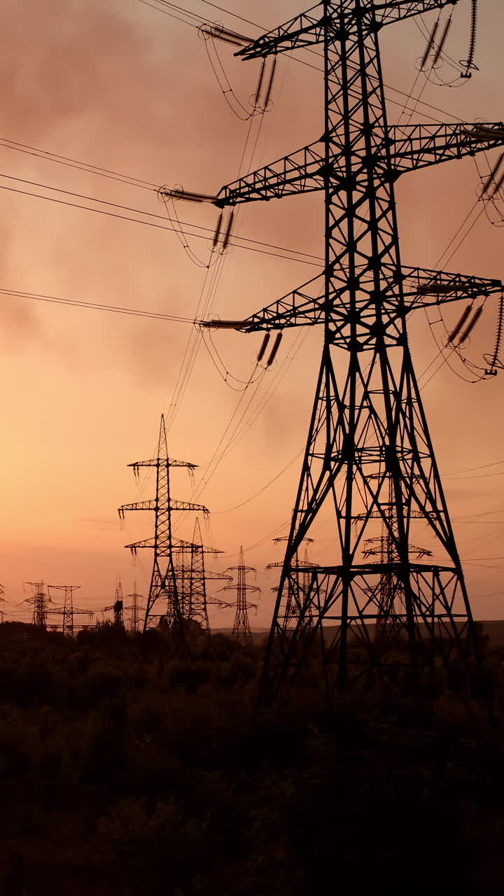 Electric towers near factory chimney with dark smoke. Transmission lines on background of harmful fumes from industry releasing from pipes at sunset. Environment pollution. Vertical video