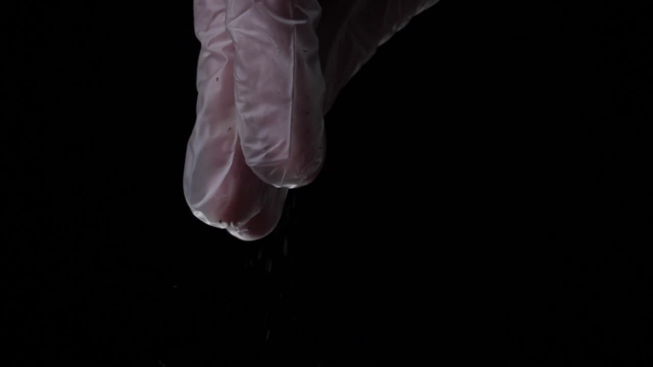 guantes rosados rociando polvo sobre un fondo negro