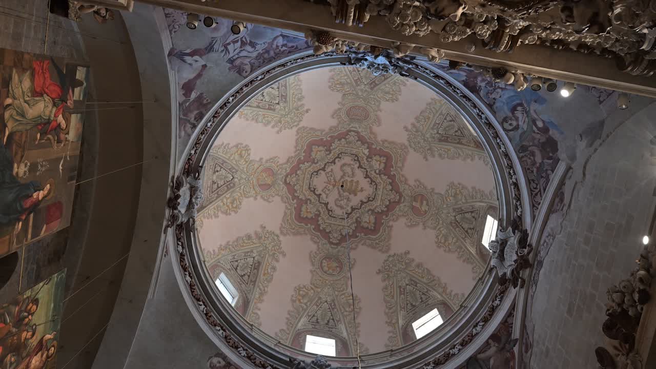 Una perspectiva vertical mirando hacia la imaginería sagrada del Señor, situada en lo alto del ornamentado techo abovedado del histórico santuario religioso con luz suave.