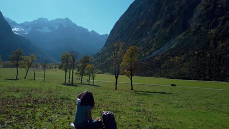 Young-woman-girl-sitting-by-colorful-vibrant-maple-trees-with-red-and-yellow-fall-leaves-in-sunny-autumn-in-the-alps-mountains-in-Tyrol,-Austria-at-scenic-Ahornboden-with-blue-sky