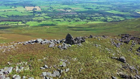 Aerial-view-of-rock-outcrop-and-ridge-line-flying-backwards-with-view-into-the-distance-over-the-South-of-Ireland-farmland