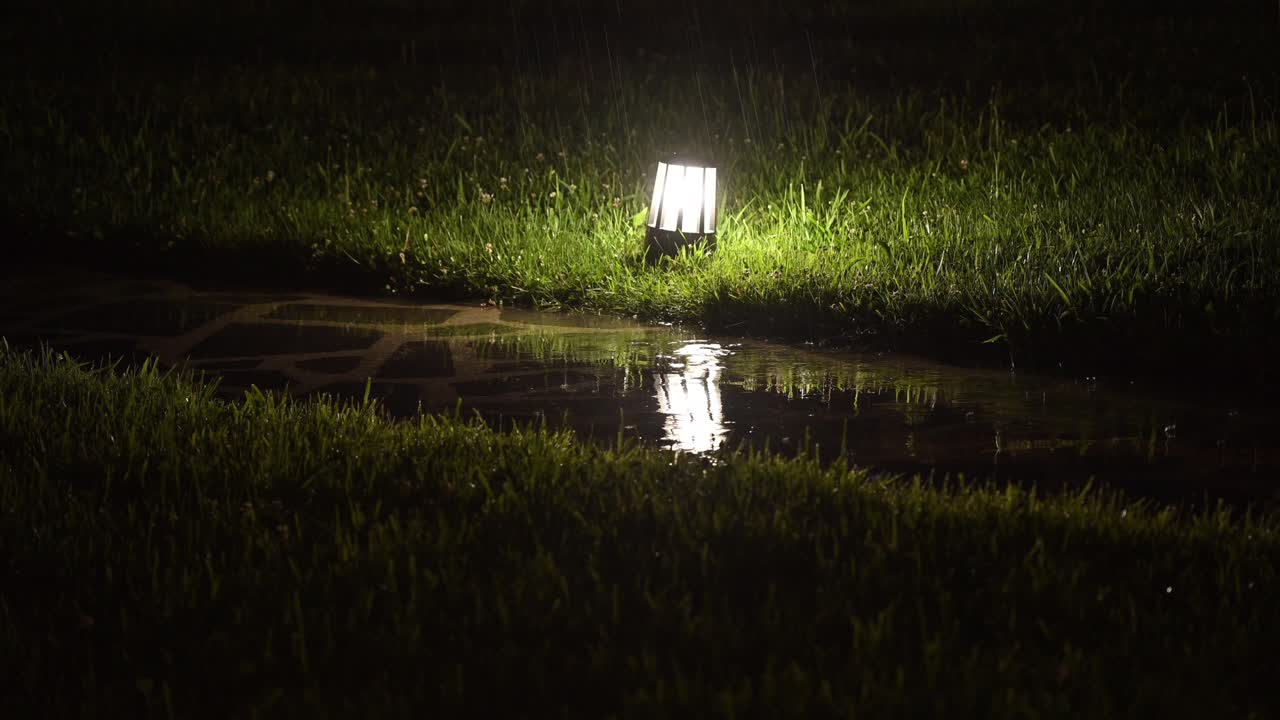 4k: escena nocturna lluviosa en georgia, con gotas de lluvia cayendo sobre la luz del jardín en el suelo