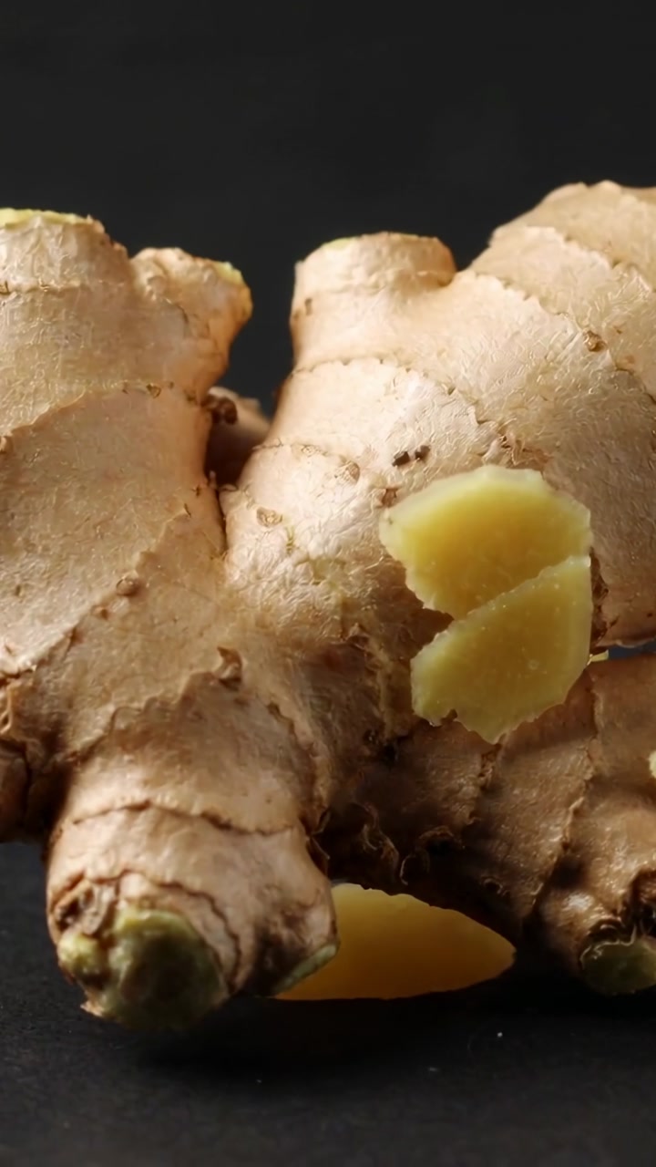 Off-screen knife slicing ginger rhizome, slices settling while glossy dollop filling frame for food