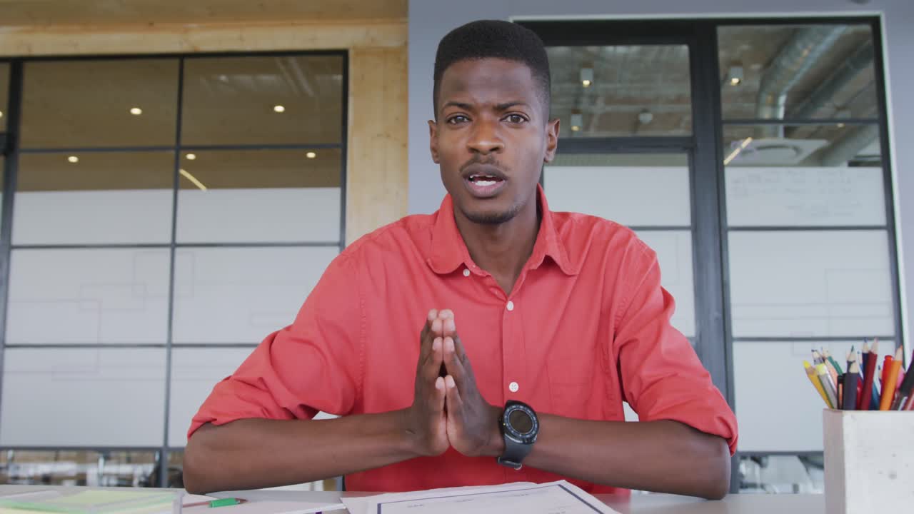 Imprenditore creativo afroamericano alla scrivania in ufficio che parla durante una videochiamata.