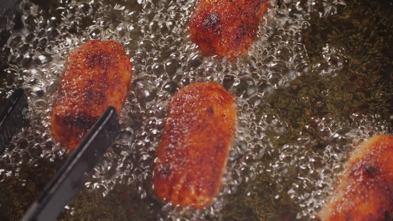 Portuguese croquettes broiling on black frying pan close-up macro. Breaded croquette of fish, potatoes and ham. Man cooking spanish food. High quality 4k footage