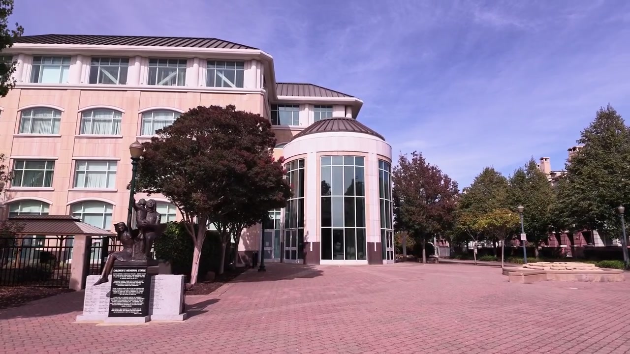 Inquadratura grandangolare che si avvicina all'ingresso principale del moderno edificio del Municipio di Hayward, situato nella Contea di Alameda, California, che mostra i suoi dettagli architettonici unici e la piazza pubblica