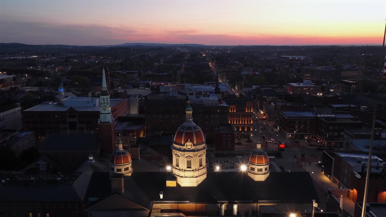 Inquadratura aerea di apertura del centro di York, Pennsylvania, al tramonto con la cupola illuminata del tribunale della contea, bandiera americana che sventola, skyline storico e un caldo crepuscolo serale sulla città negli USA. Ampia inquadratura.