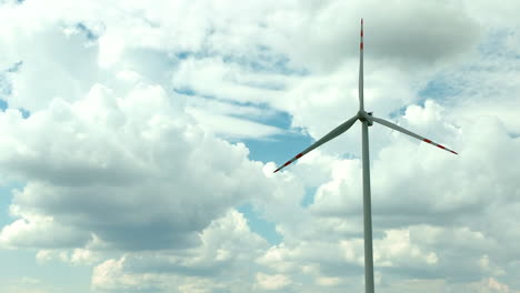 Aerial-footage-showing-a-single-wind-turbine-against-a-backdrop-of-dramatic,-fluffy-clouds-and-a-bright-blue-sky