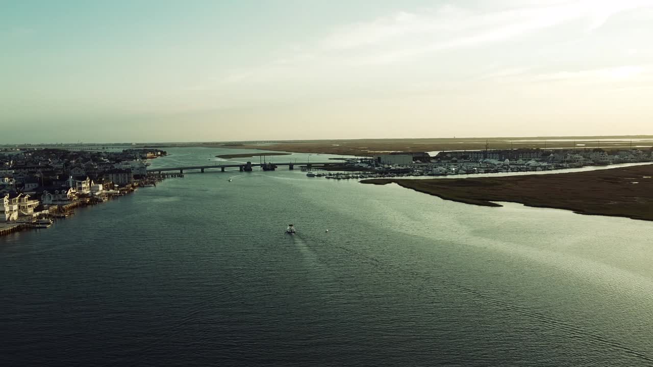 뉴저지 스톤하버에 있는 다리로 향하는 항구 너머의 아리엘은 골든 아워 동안 중앙에 작은 보트가 있습니다.