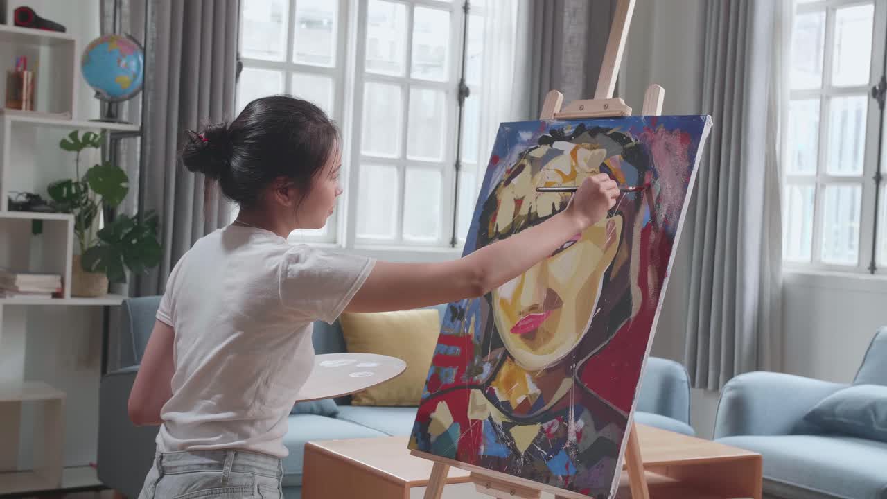 Medium Shot Side View Of An Asian Artist Girl Holding Paintbrush Mixed Colour And Painting A Girl'S Ear On The Canvas