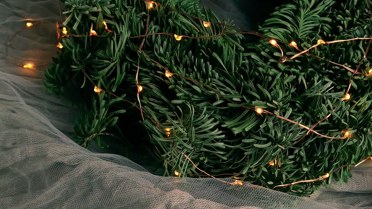 olhando para uma guirlanda de natal decorativa feita de agulhas de pinheiro e luzes de fada em uma cama de tecido fino e transparente