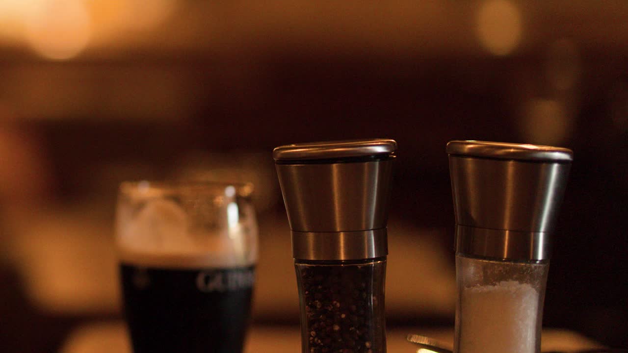 Dark beer and metal shakers on rustic bar table, shallow focus, warm ambient bokeh lighting