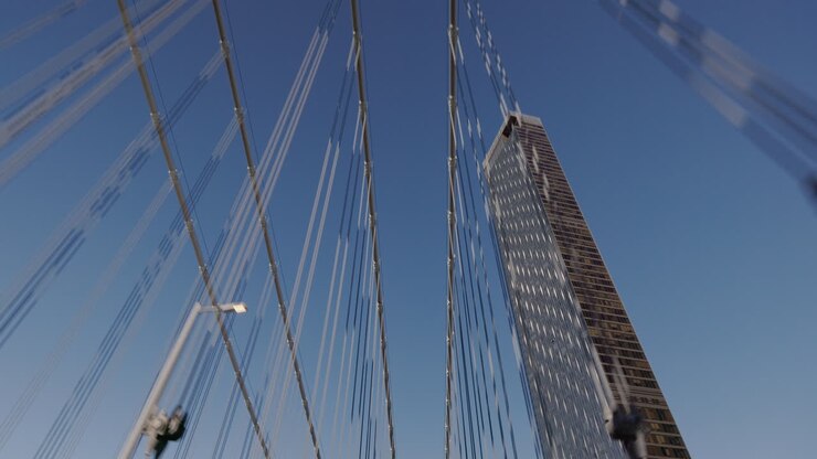 Dynamic close view of Manhattan Bridge tower with nearby skyscraper in New York City, fast forward motion under suspension cables, USA