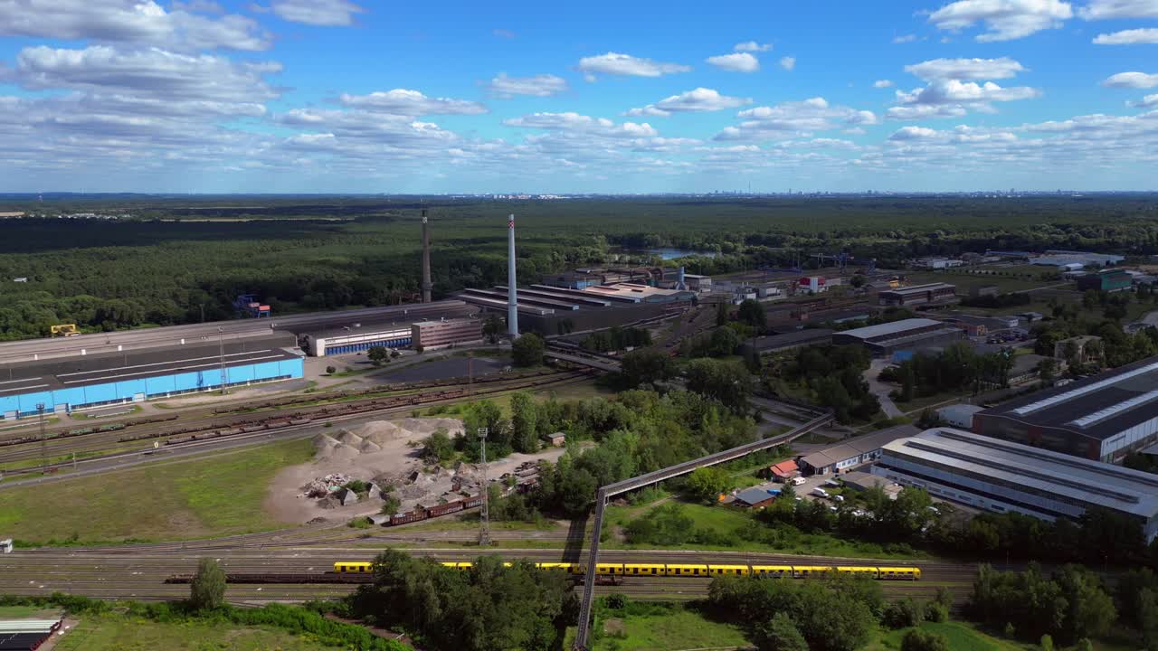 Acciaieria di Hennigsdorf con ciminiere, magazzini, ferrovia, vicino al fiume e alla foresta in estate. Fluido volo aereo con drone che vola all'indietro