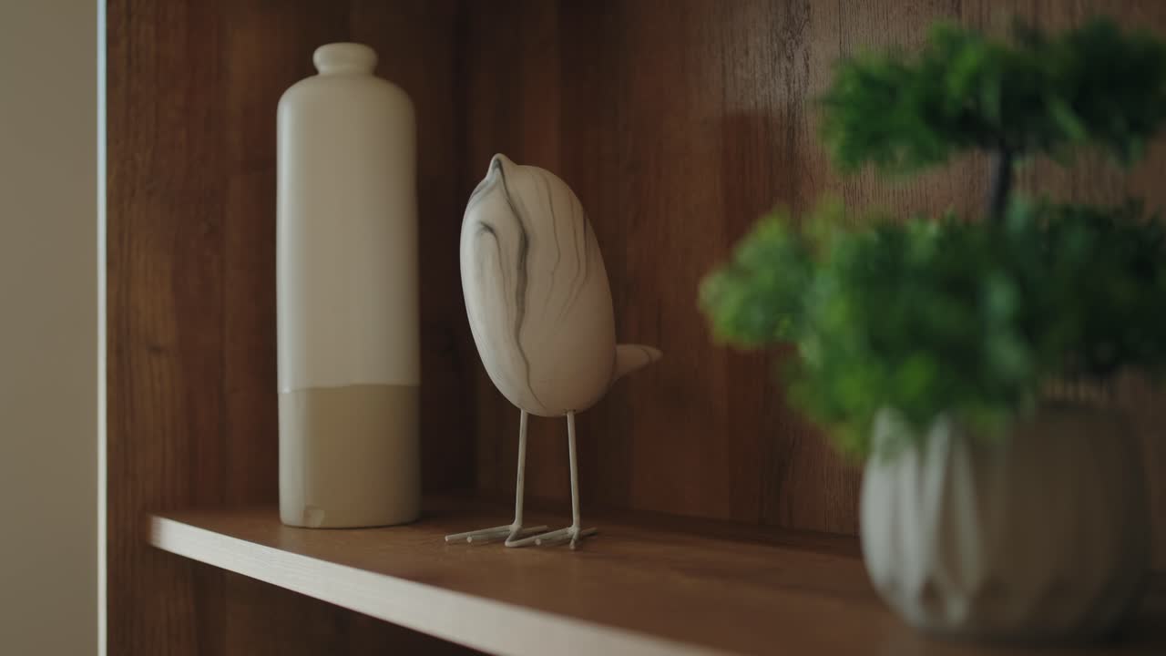 Close up of ceramic vase, bird sculpture, and potted plant on wooden shelf for interior design