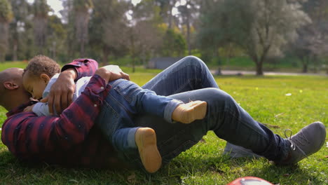 father lying on grass, catching mixed-race son, playing together