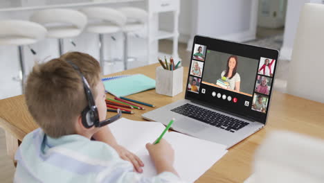 schoolboy using laptop for online lesson at home, with diverse teacher and class on screen