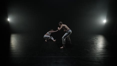 capoeira fighters performing dynamic moves on stage. martial arts, dance, and acrobatics in action. bare-chested athletes showcasing strength, flexibility, and technique under spotlights