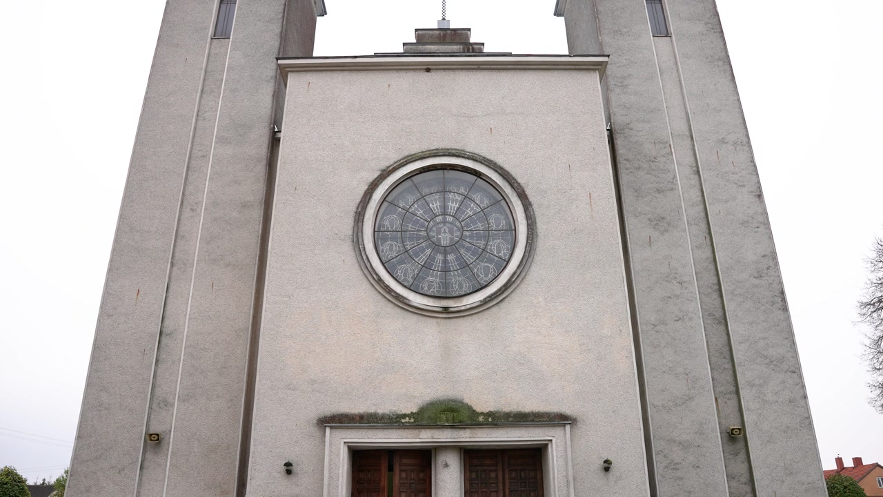 A serene view of Pilviškiai Holy Trinity Church's facade in Lithuania, with intricate architecture captured on a cloudy day. No people are visible, emphasizing the historic structure.